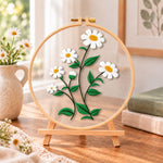 White daisies with green leaves embroidery kit finished hoop displayed on a wooden stand as cozy tabletop decor