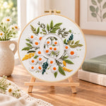 White daisy cluster and letter q embroidery kit finished hoop displayed on a wooden stand as cosy tabletop decor