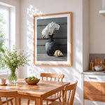 White orchids in a dark vase with shell cross stitch artwork displayed on wall as home decor