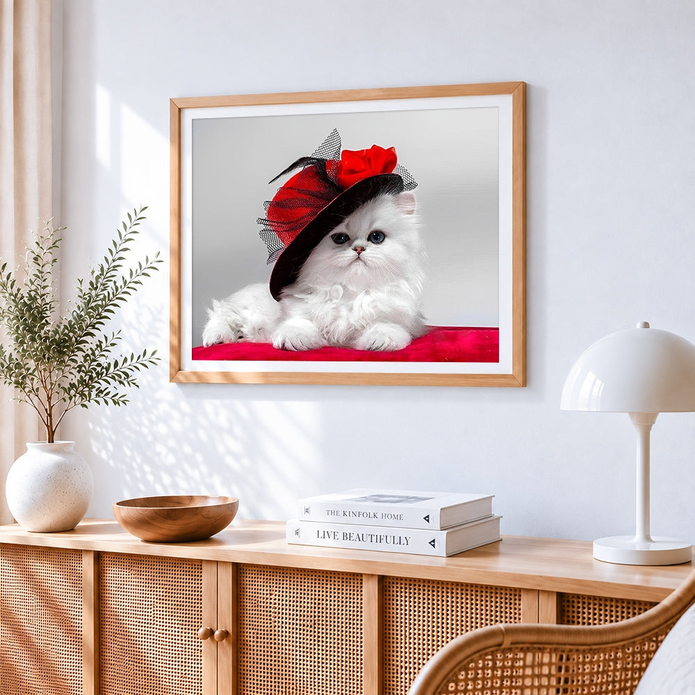 White persian kitten in red hat cross stitch artwork displayed on wall as home decor