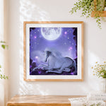 Finished white unicorn resting under a full moon cross stitch artwork displayed