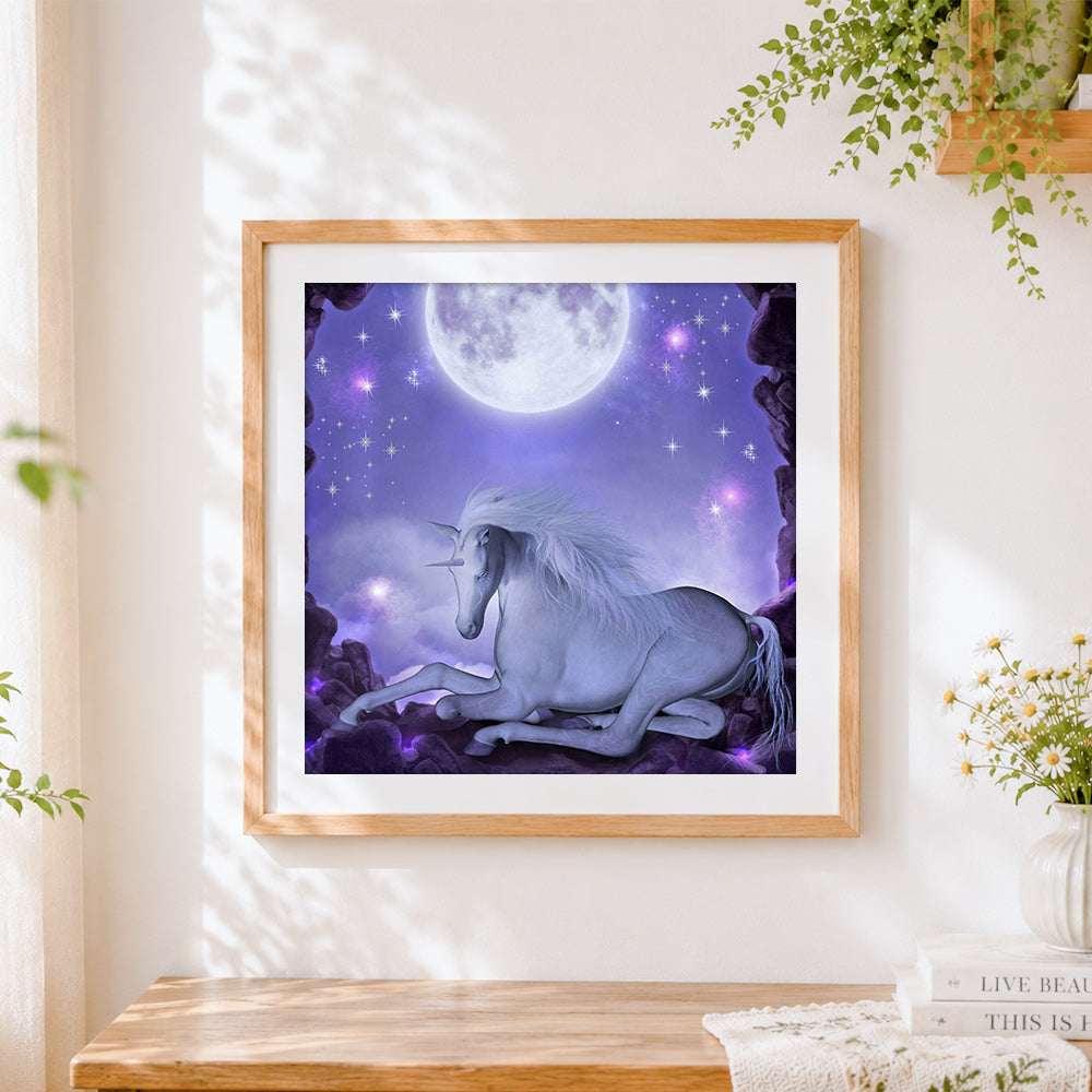 Finished white unicorn resting under a full moon cross stitch artwork displayed