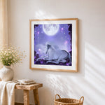 White unicorn resting under a full moon cross stitch artwork displayed on wall as home decor