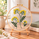 Yellow wildflower bouquet embroidery kit finished hoop displayed on a wooden stand as cozy tabletop decor