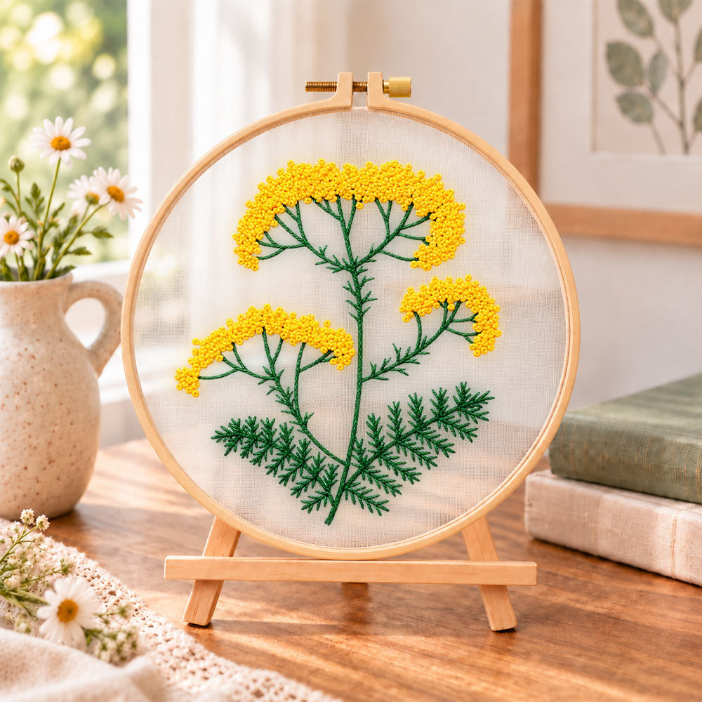 Yellow wildflower stem embroidery kit finished hoop displayed on a wooden stand as cozy tabletop decor